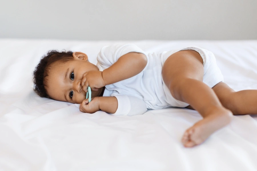 Teething African American baby lays in bed